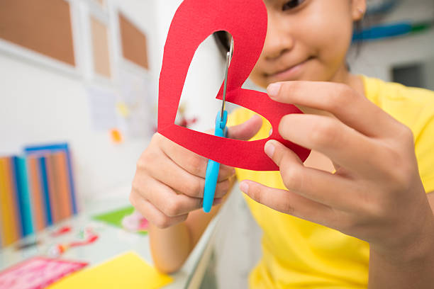 Girl cutting out paper heart, selective focus